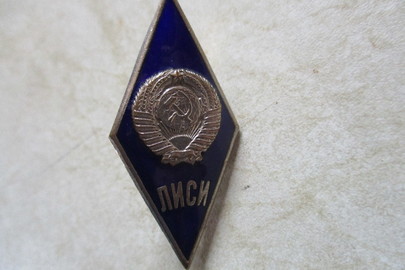 Нагрудний знак у вигляді ромба, в центрі якого на синьому фоні є зображення герба СРСР, виконані з металу білого кольору, під зображеннями є надпис «ЛИСИ»